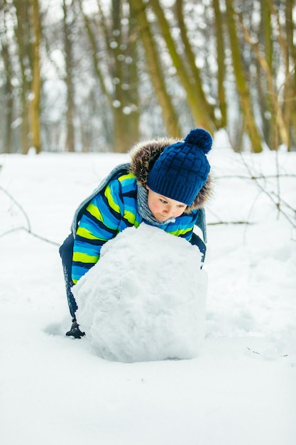 Niño lindo haciendo muñeco de nieve rodando gran bola de nieve