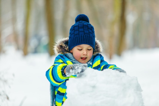 Niño lindo haciendo muñeco de nieve rodando gran bola de nieve