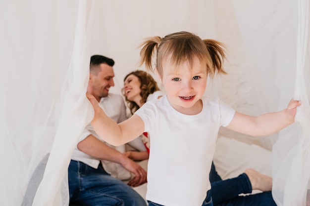 Niño lindo hija y papá cosquillas mamá divirtiéndose bien jugando juntos en casa, padres felices y niña pequeña disfrutando de una actividad divertida y comunicación, familia riendo relajante