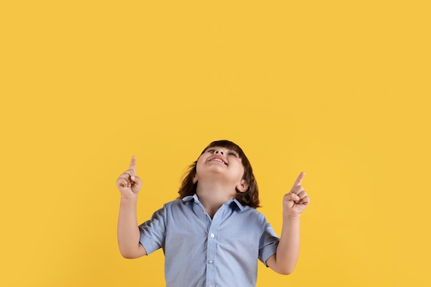 Un niño lindo mirando hacia arriba y señalando con ambas manos disfrutando de un interesante espacio vacío de fondo naranja promocional