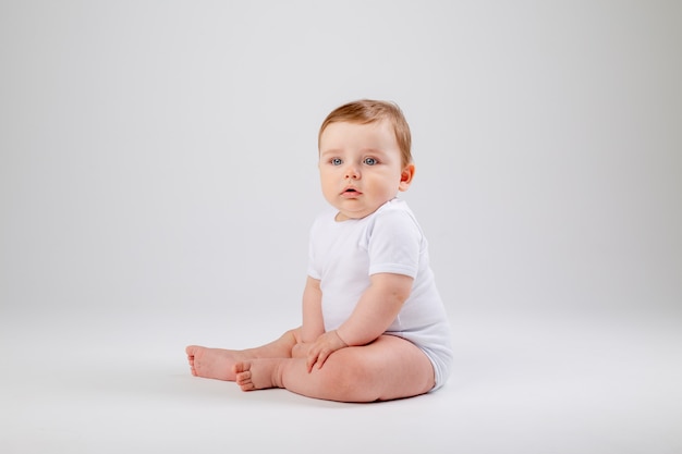 Niño lindo niño de 8 meses en traje blanco se sienta