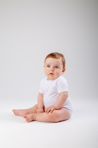 Niño lindo niño de 8 meses en traje blanco se sienta