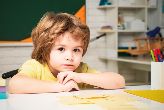 Niño lindo niño en el aula cerca del escritorio de la pizarra niños de la escuela primaria