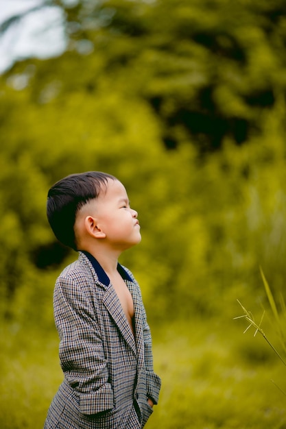 Un niño lindo Un niño bien vestido con traje en un patio trasero con césped y buscando algo interesante