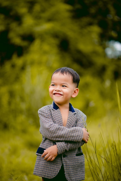 Un niño lindo Un niño bien vestido con traje en un patio trasero con césped y buscando algo interesante