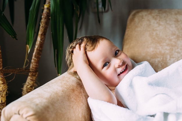 Niño lindo con ojos azules envuelto en una toalla blanca