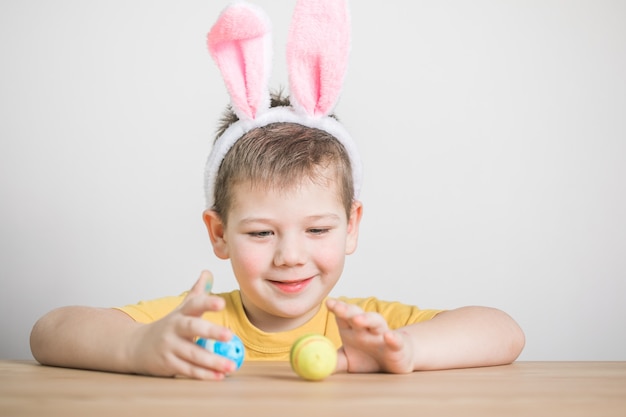 Niño lindo con orejas de conejo el día de Pascua. Niño sosteniendo huevos pintados sobre fondo blanco.