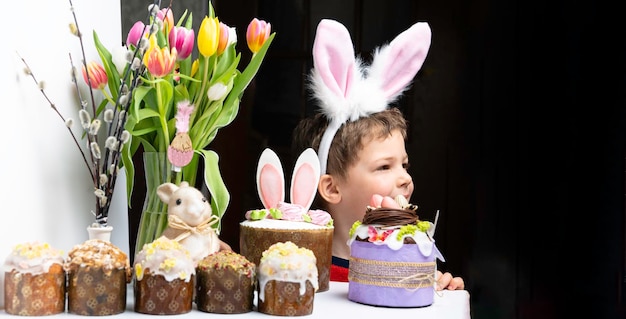 Un niño lindo con orejas de conejo mirando un sabroso pastel dulce de pascua