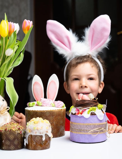Un niño lindo con orejas de conejo mirando un sabroso pastel dulce de pascua