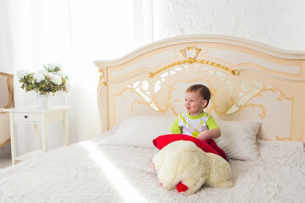 Niño lindo con osito de peluche en el dormitorio