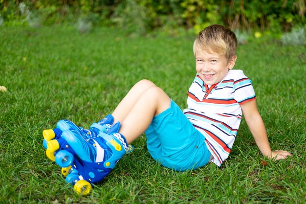 Un niño lindo en patines está sentado en el césped sonriendo mirando a la cámara el concepto de juegos deportivos al aire libre juegos activos