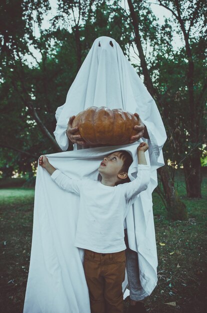 Foto un niño lindo con una persona vestida con un disfraz de fantasma en el parque al atardecer durante halloween