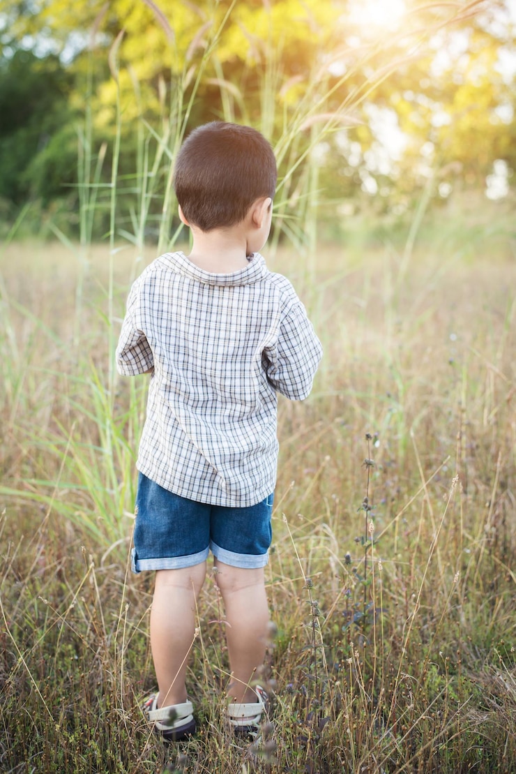 Foto un niño lindo de pie con las manos juntas en un campo de hierba durante un día soleado