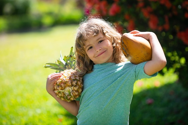 Niño lindo con piña y coco en el jardín tropical frutas tropicales frescas para niños estilo de vida saludable ...