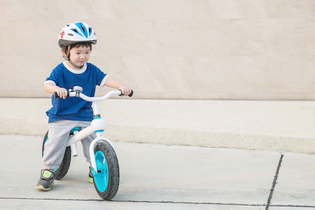 El niño lindo del primer monta una bicicleta en piso del cemento en el aparcamiento