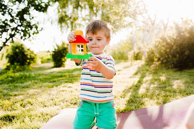 Niño lindo que sostiene una casa de juguete en el jardín y parece pensativo.