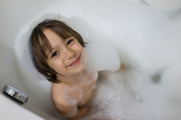 Niño lindo que tiene baño de burbujas