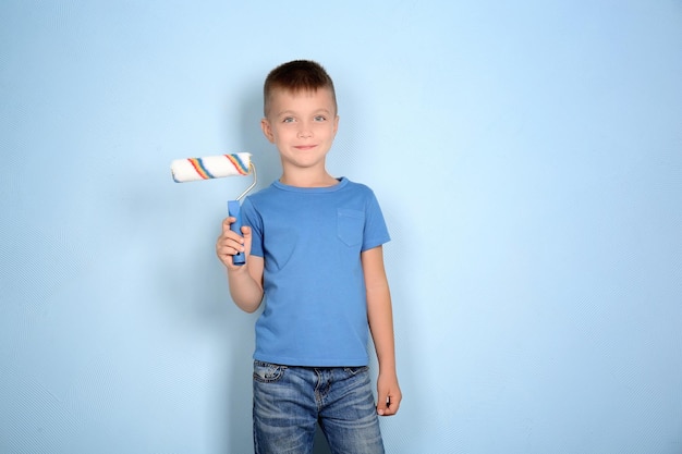 Niño lindo con rodillo de pintura sobre fondo azul claro