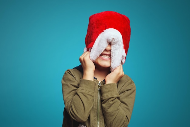 Niño lindo en ropa casual que cubre la cara con sombrero rojo de navidad