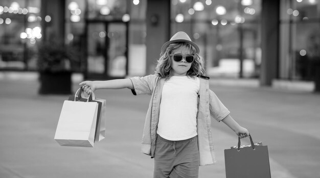 Foto un niño lindo con ropa de moda de verano va de compras un niño feliz con paquetes de compras en las manos