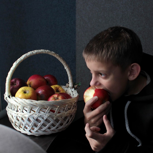 Foto un niño lindo y satisfecho está sentado junto a una canasta de manzanas rojas y amarillas jugosas