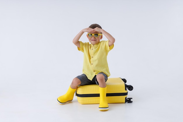 Niño lindo sentado en una bolsa de viaje amarilla