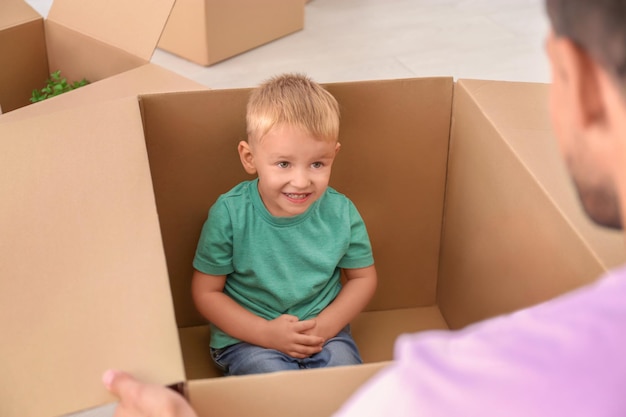 Un niño lindo sentado en una caja móvil y jugando con su padre en casa