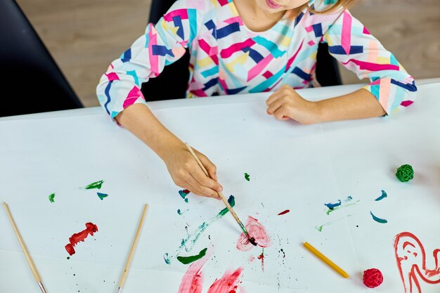 Niño lindo sentado en la mesa y dibujo corazón rojo sobre papel blanco