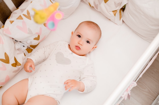 Niño lindo se sienta en la cama de bebé en casa