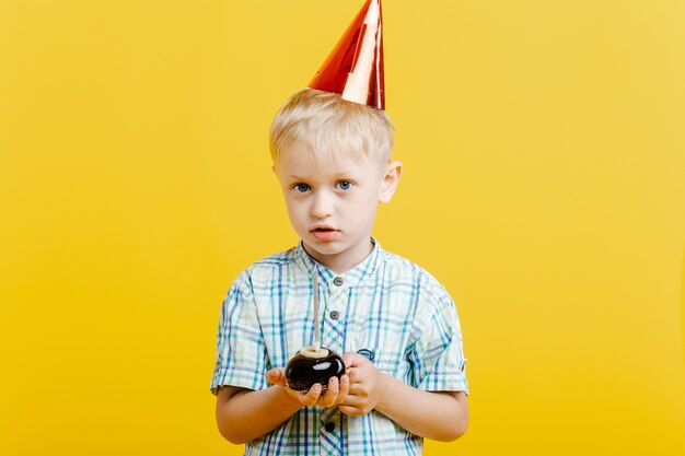 Niño lindo con sombrero de cumpleaños y pastel en amarillo