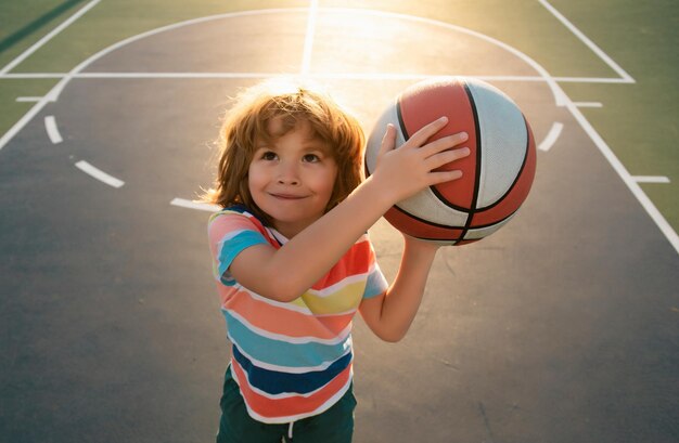 Un niño lindo y sonriente juega al baloncesto. Niños activos disfrutando de un juego al aire libre con la pelota de baloncesto en la vista superior.