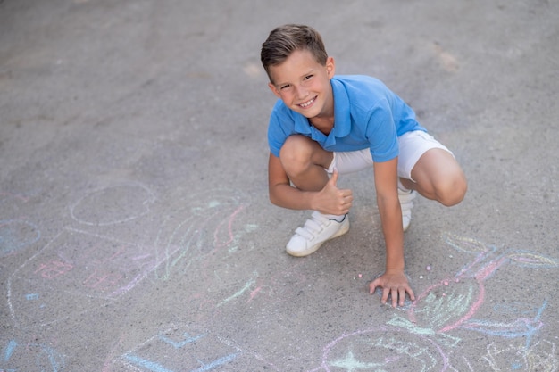 Un niño lindo y sonriente de pelo corto sentado en cuclillas haciendo una señal de aprobación ante la cámara