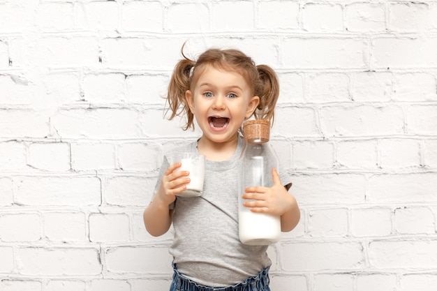 Niño lindo sorprendido con cara de expresión y bigote de leche en los labios sobre pared de ladrillo blanco