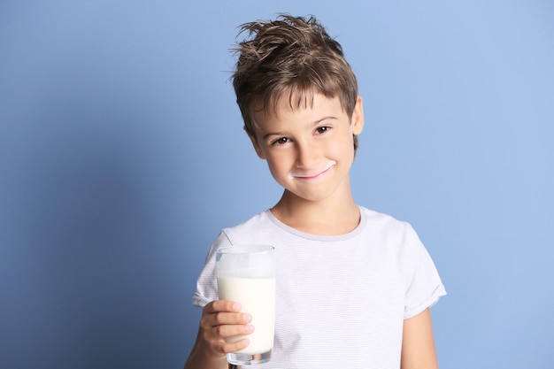 Foto niño lindo sosteniendo un vaso de leche en la pared azul