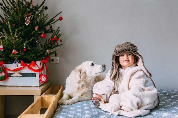 Niño lindo y su labrador retriever en casa en la cama cerca del árbol de Navidad