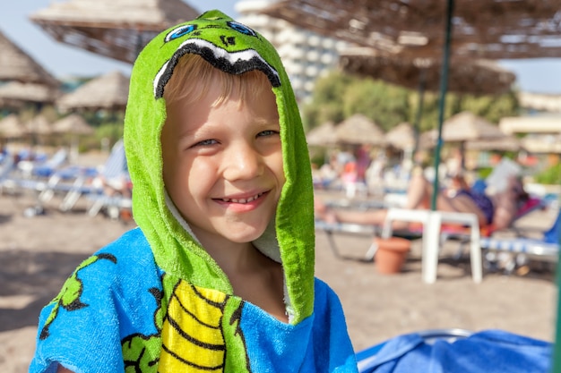 Niño lindo con una toalla divertida en la playa