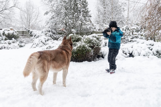 Un niño lindo toma fotos de un perro husky en el parque de invierno