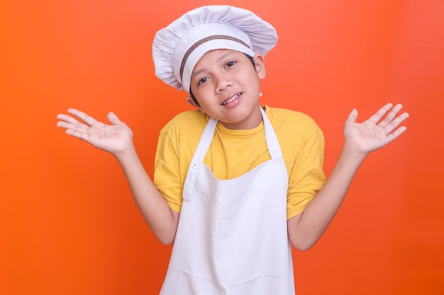 Niño lindo con uniforme de cocina sin idea y confundido con los brazos abiertos sin idea y dudoso