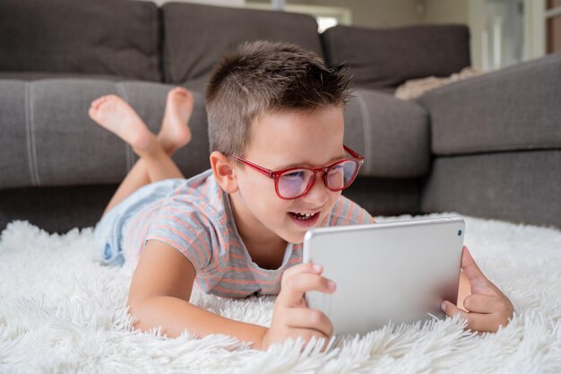 Un niño lindo ve dibujos animados en una tableta digital El niño yace en el suelo riéndose usando un dispositivo electrónico Ocio interior para niños