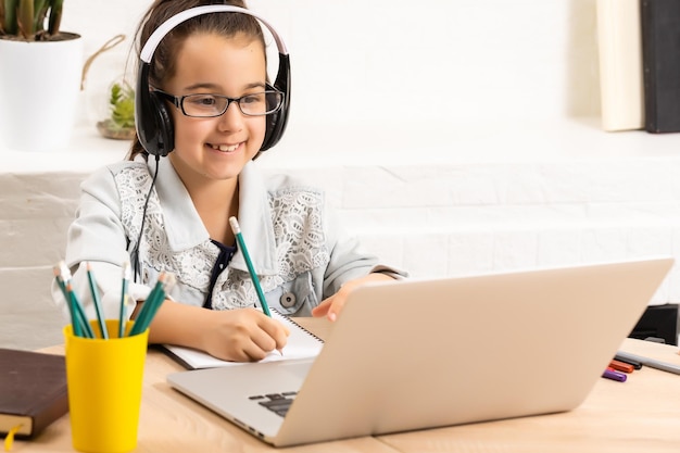 Niño en línea. Una niña usa un chat de video portátil para comunicar el aprendizaje mientras está sentada en una mesa en casa.