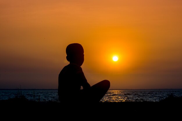 Un niño lisiado sentado en el río mirando la puesta de sol Un día que termina Triste historia