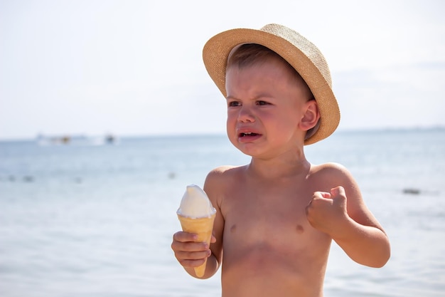 El niño llora y come helado en la playa.