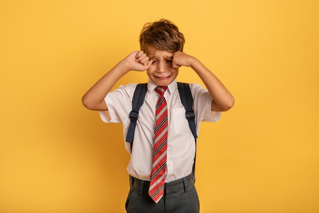 El niño llora porque no quiere ir a la escuela. Fondo amarillo