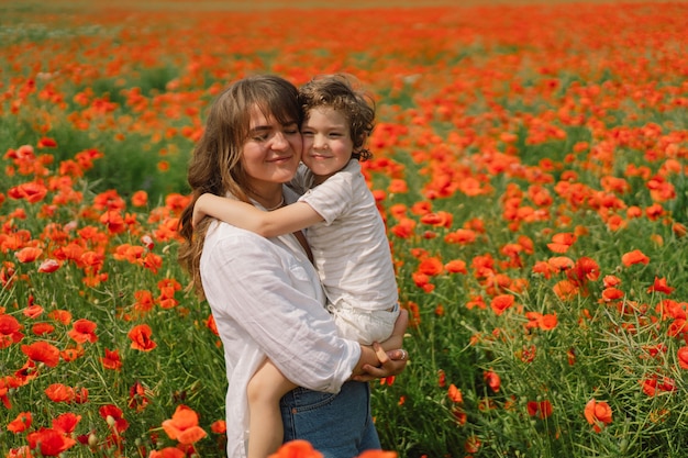 El niño y la madre están jugando en un hermoso campo de amapolas rojas.