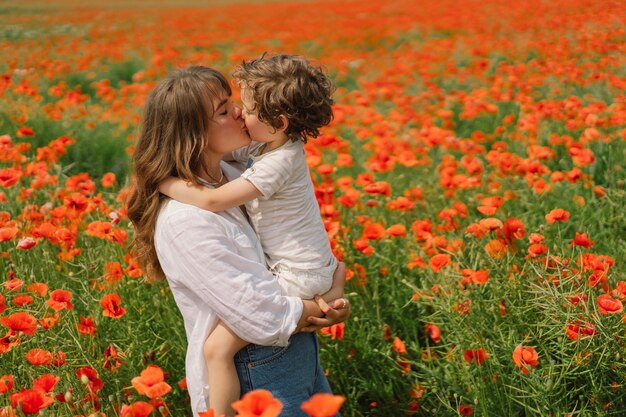 El niño y la madre están jugando en un hermoso campo de amapolas rojas.