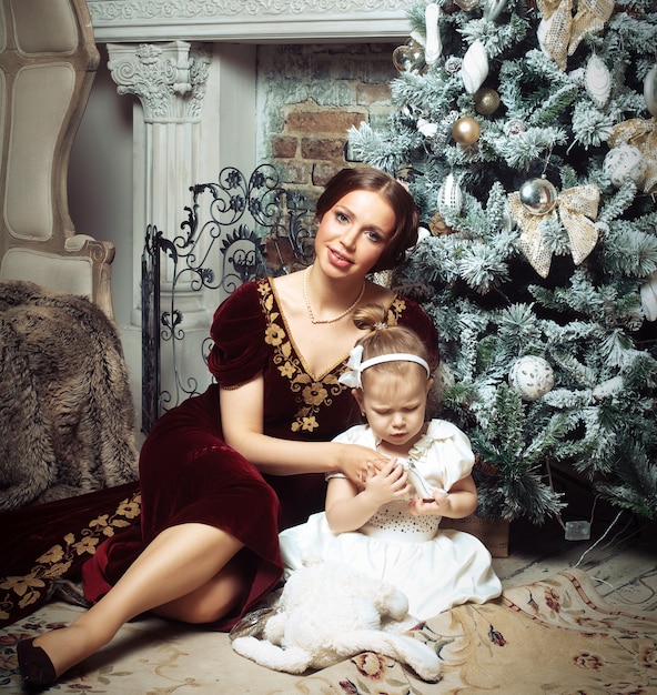 Niño con madre sentada cerca de árbol de Navidad.