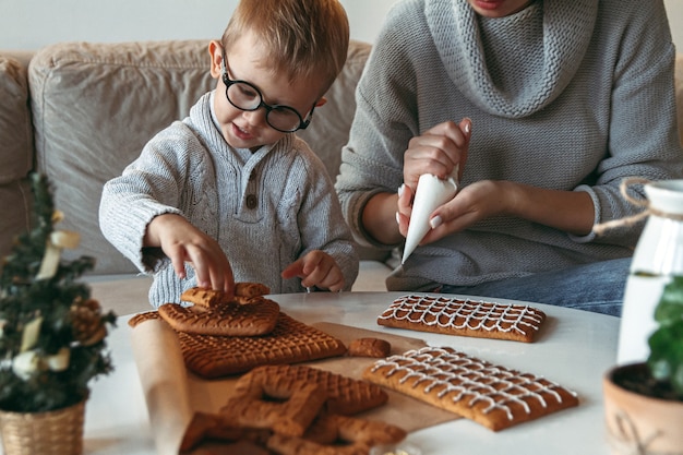 Niño con mamá decorar la casa de pan de jengibre de navidad juntos