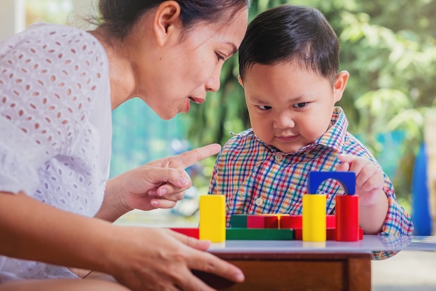 Niño y mamá jugando con bloques de colores de madera El niño pequeño tiene la intención de construir una torre con bloques de colores de madera Juguetes educativos y concepto de niños de aprendizaje en casa