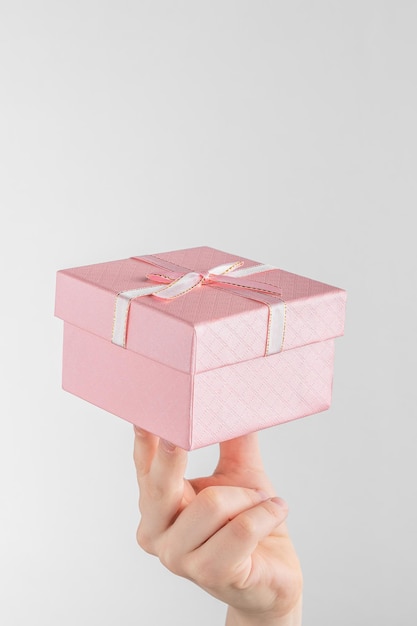 Foto niño mano sujetando caja de regalo con lazo rosa fondo blanco y gris con espacio de copia