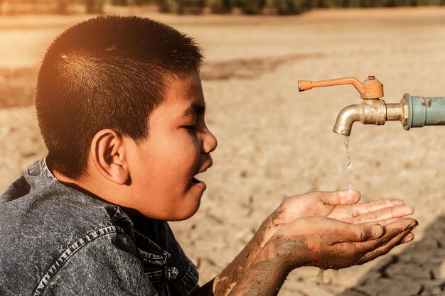 Foto niño con las manos cubiertas bajo el grifo en tierra seca